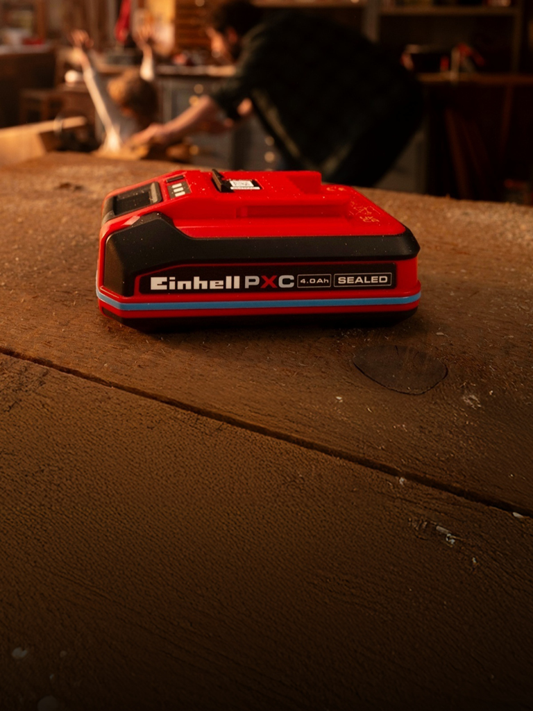 Batería Einhell Power X-Change 4.0Ah SELLADA en un banco de trabajo de madera, que muestra un anillo y una etiqueta azules. 