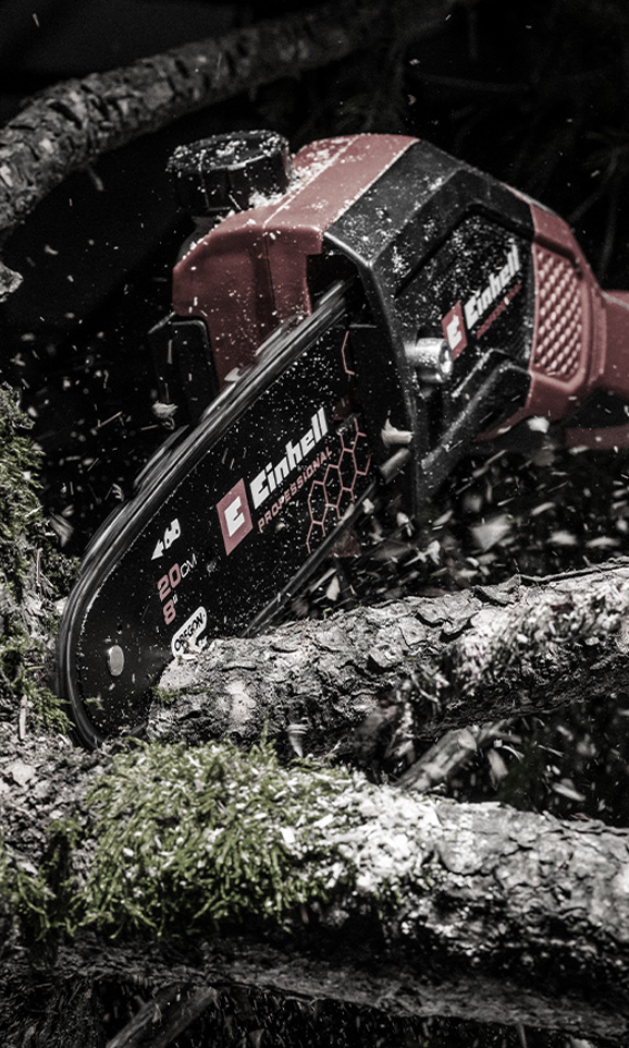 Motosierra Einhell cortando una rama, con aserrín volando en el aire.
