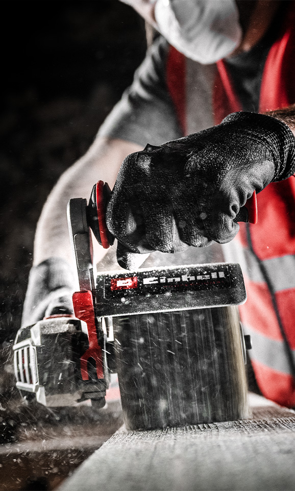 Persona lijando una tabla de madera con una lijadora Einhell roja, con partículas de polvo en el aire.
