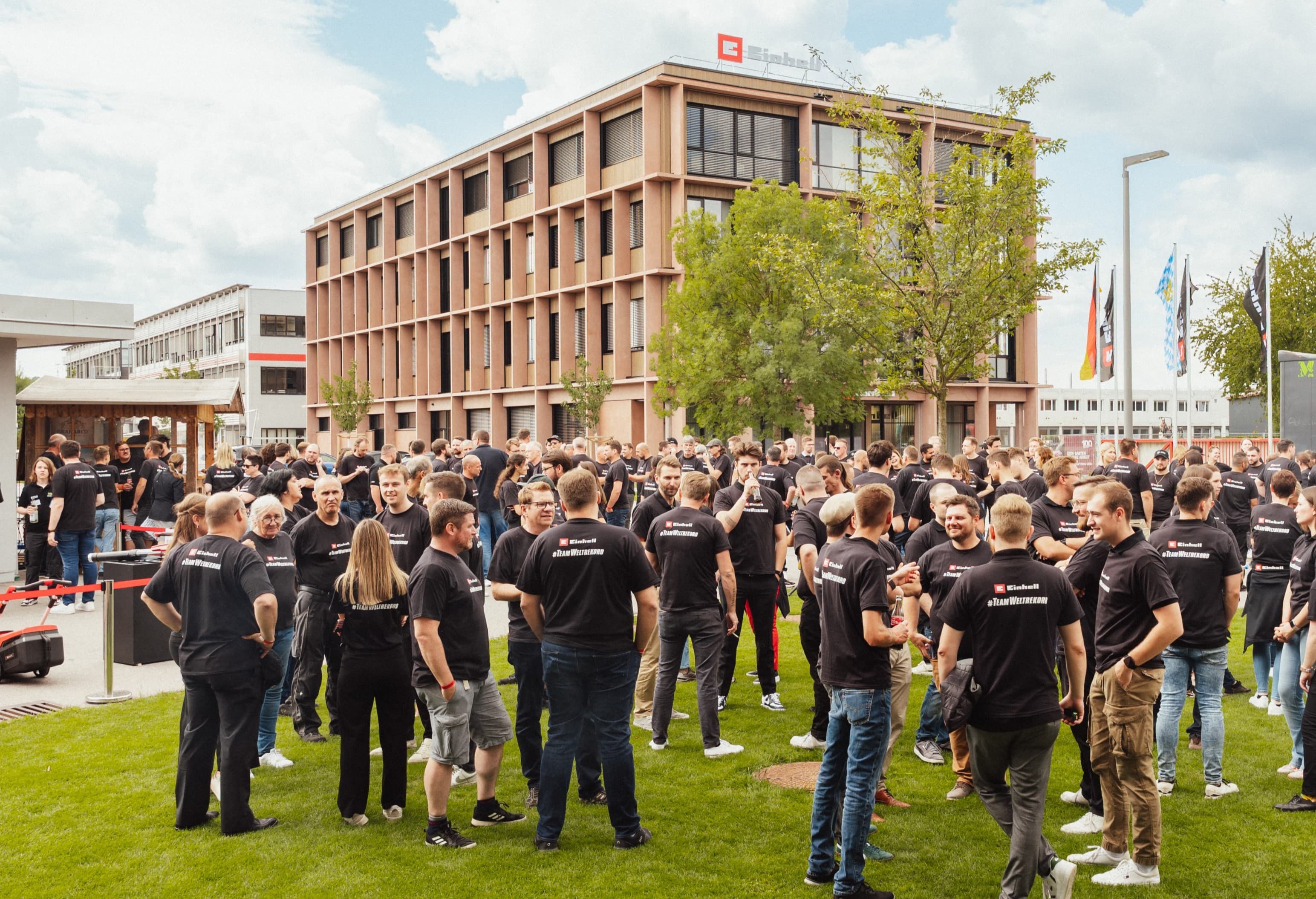 Many people in black Einhell shirts with the slogan "#TeamWeltrekord" gather on company grounds.