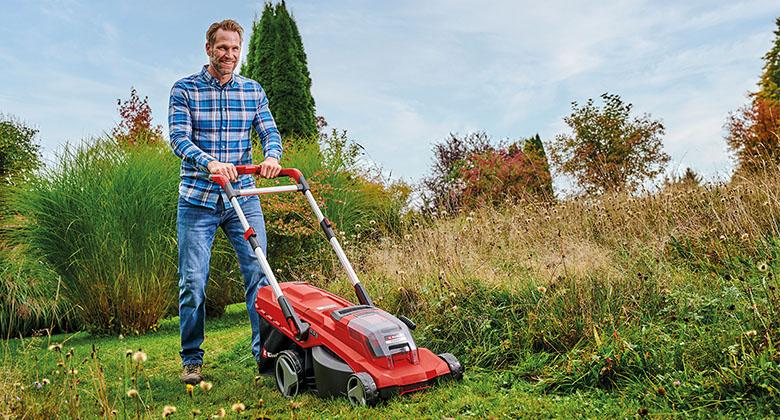 A man mowing tall grass with a cordless lawnmower.