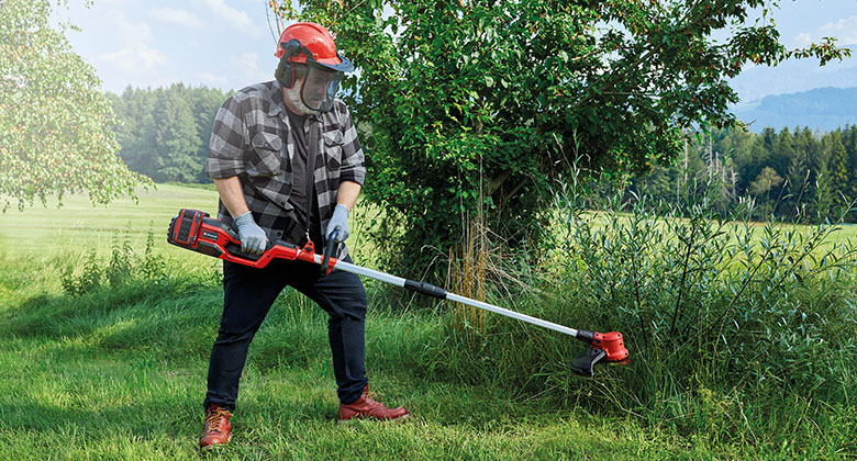 A man cuts tall grass with a battery-powered scythe from Einhell