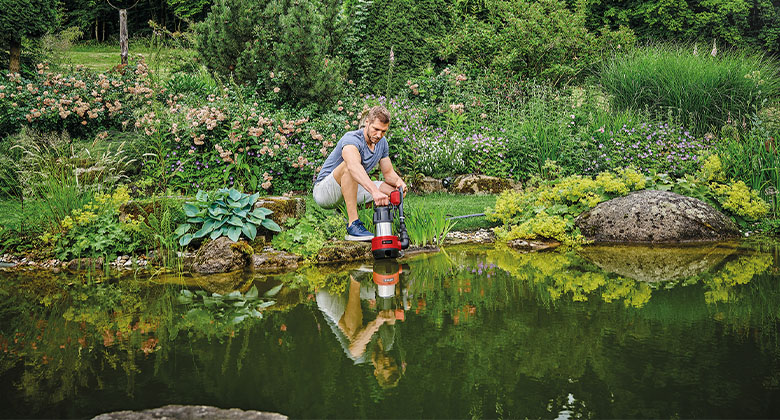  A man draining a dirty water pump into a large pond to pump the water out.