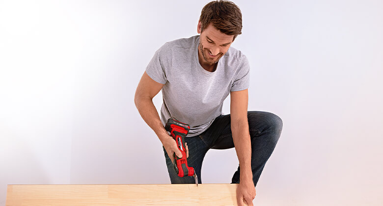 A man cutting into a wooden beam with an Einhell multifunction tool.